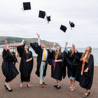 Myfyrwyr yn dathlu graddio ar y promenâd yn Llandudno