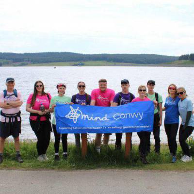 Students, lecturers and Conwy Mind staff holding a Mind Conwy banner at Llyn Brenig