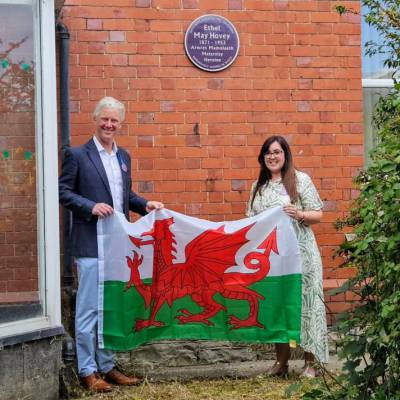 Coleg Llandrillo lecturer Gemma Campbell with Chris Winchester, holding a Wales flag at the unveiling of a plaque dedicated to Ethel Hovey