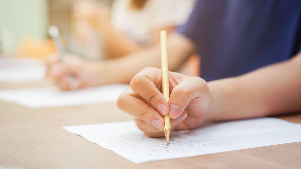 Llaw myfyriwr agos yn defnyddio pensil ar gyfer arholiad testun